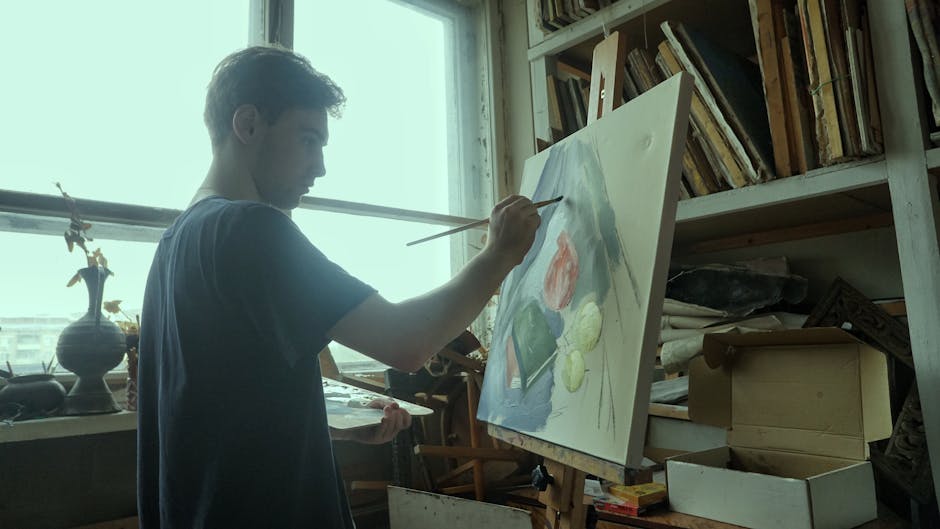 A young man painting on a canvas in a sunlit art studio.