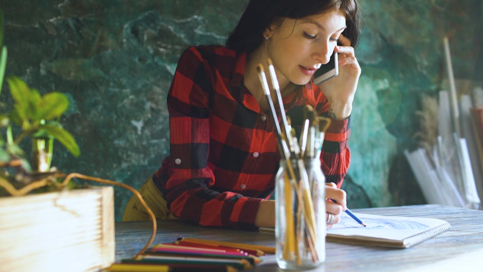 Woman multitasking in an art studio, sketching while answering a phone call.