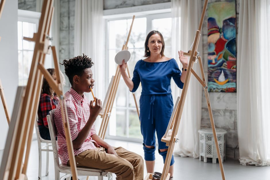 Instructor guiding children in a creative art class with easels.