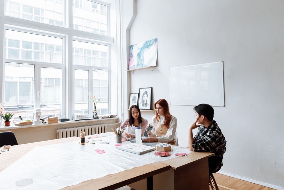 Three individuals engage in a creative art session in a modern studio with natural light.