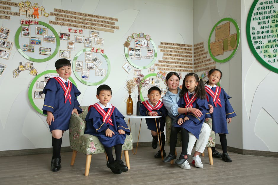 Children in kindergarten graduation attire posing indoors with their teacher.